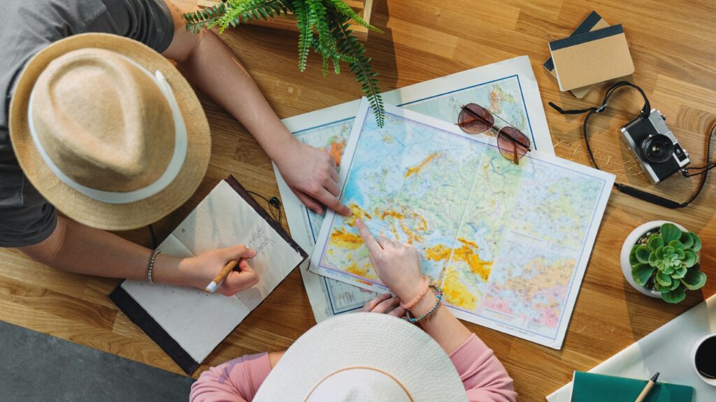 Aerial shot of two people wearing hats and looking at a map with pen and paper in hand.