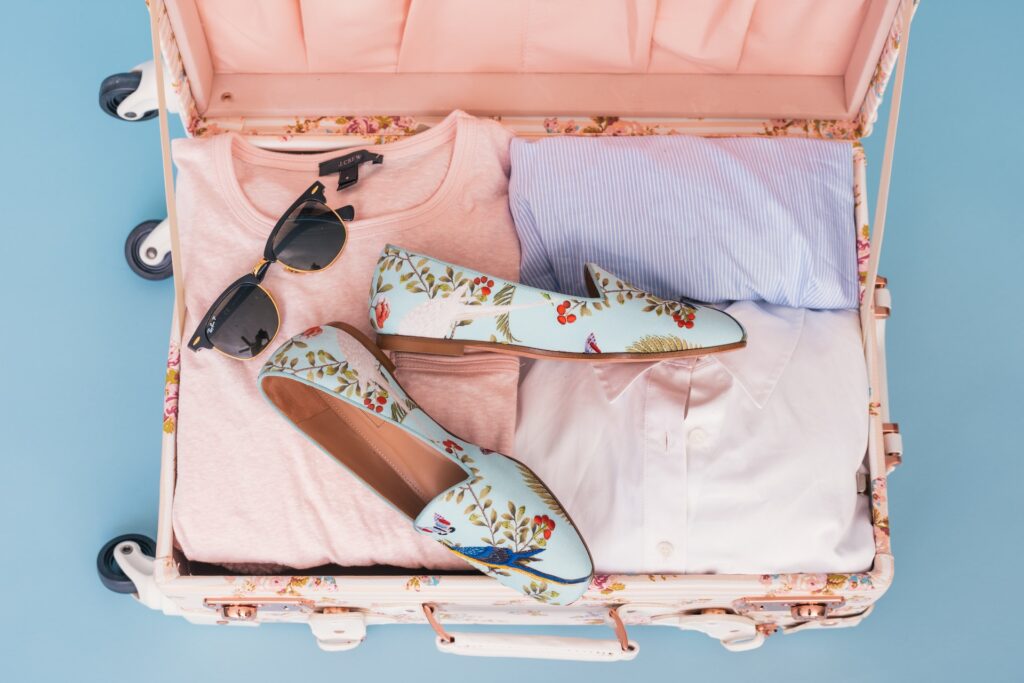 Image of an open suitcase, packed with clothes, shoes and sunglasses