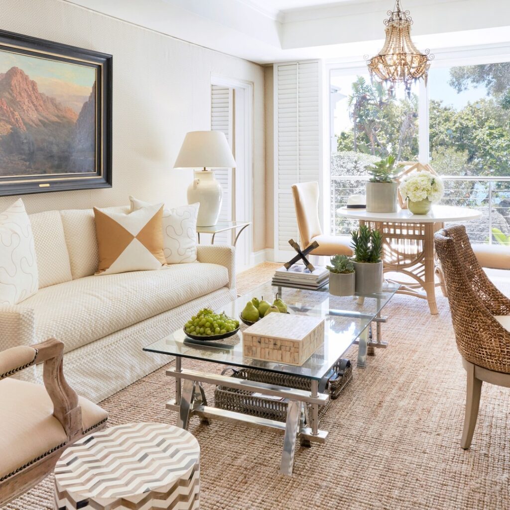 Image of a room interior at 12 Apostles Hotel, with a glass coffee table, a landscape painting on the wall and ceiling height windows overlooking gardens at the end of the room