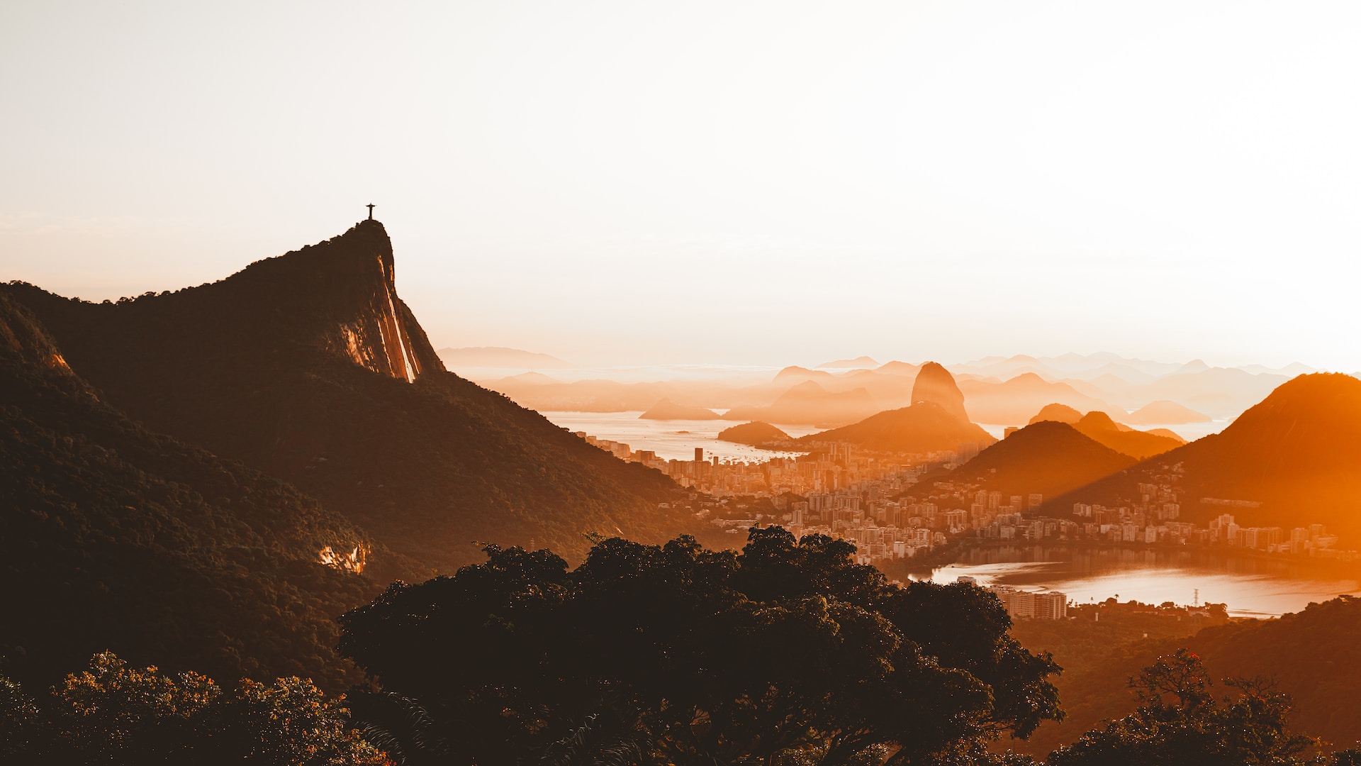 View of Rio de Janeiro at sunset, looking across the city's mountainous landscape, with the Christ the Redeemer statue in the middle ground