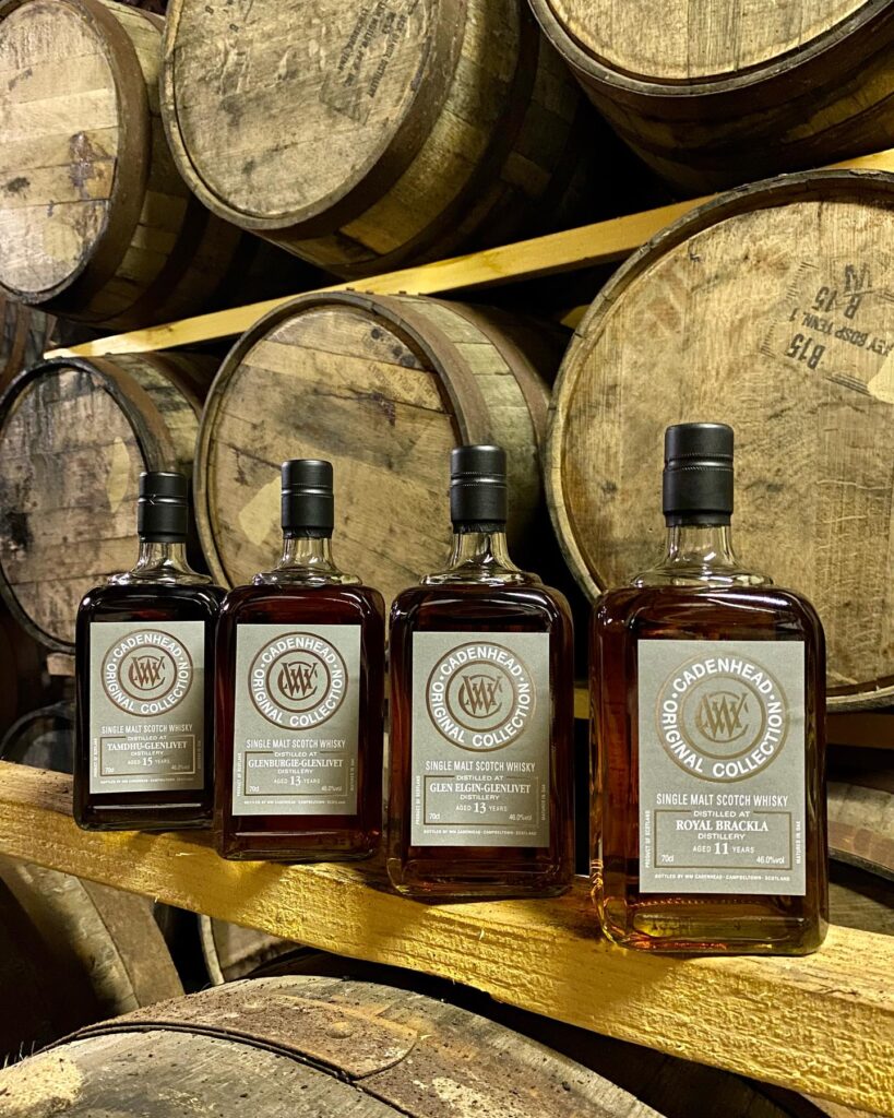 Four whisky bottles stand in front of barrels and casks.