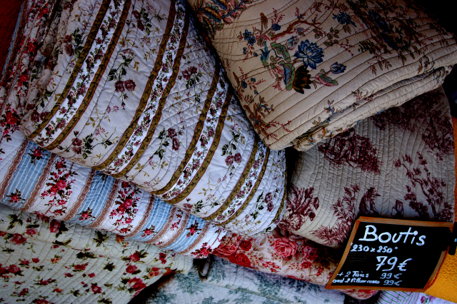 A pile of intricately patterned quilts, with a variety of colours 