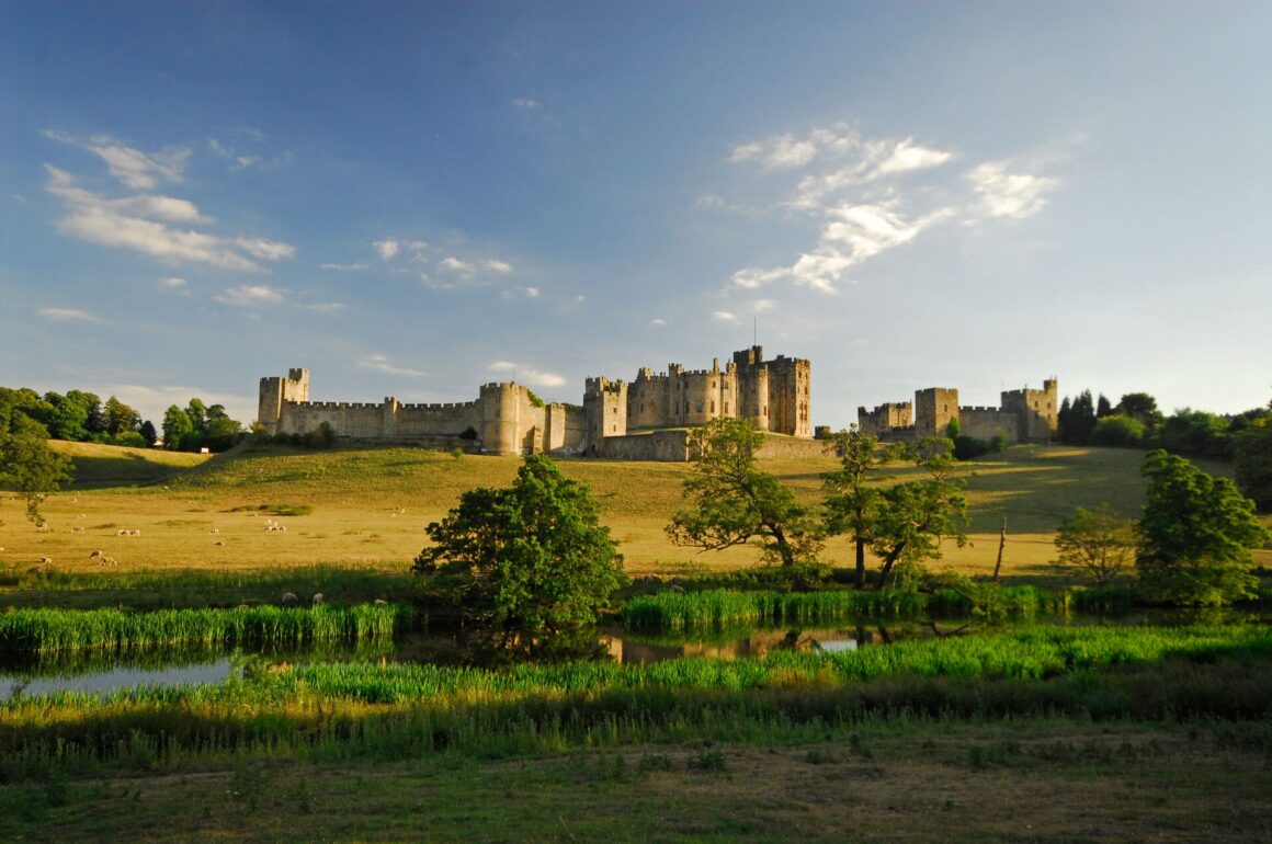 Photo of Alnwick Castle on a hilltop, in late golden sunlight, surrounded by fields