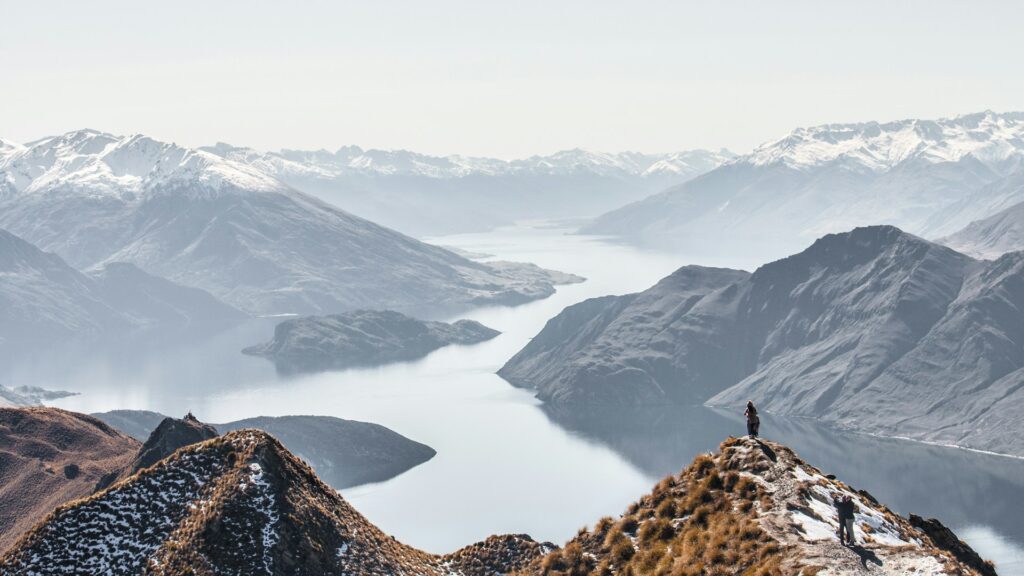 Travelers standing on top of a mountain peak, overlooking lakes and other mountains in New Zealand