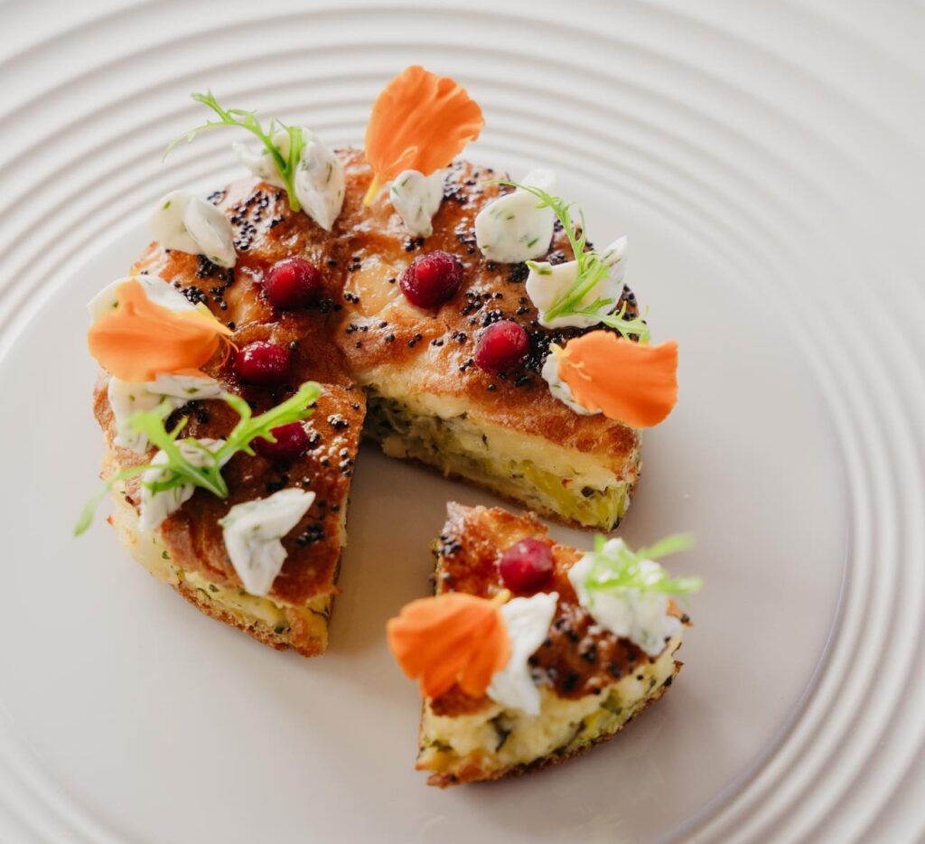 A stunningly presented seafood tart with red and orange fruit and flower garnish served on a white plate