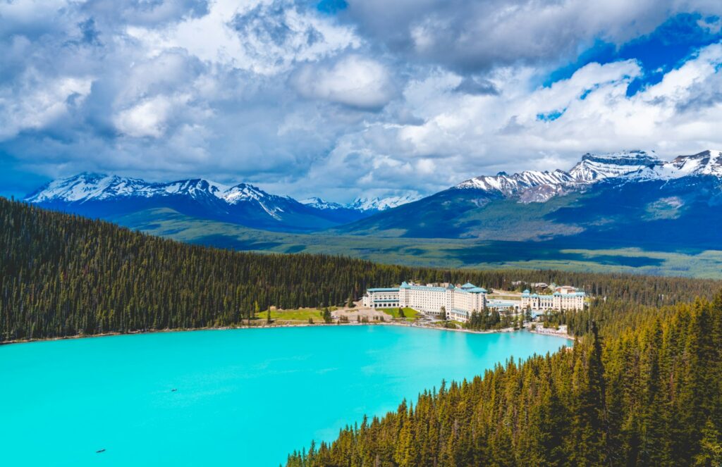 Grand hotel overlooking a bright blue glacial lake, surrounded by pine forest with mountains in the background