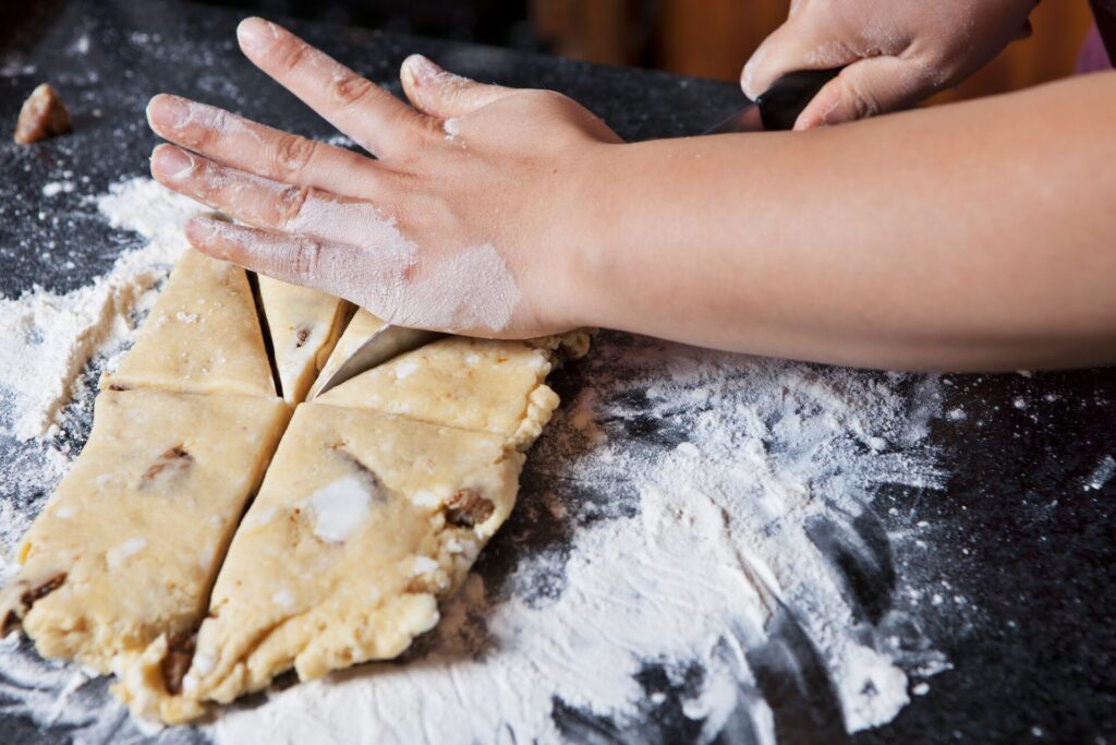 Dough is kneaded by hands, on flour on a dark surface