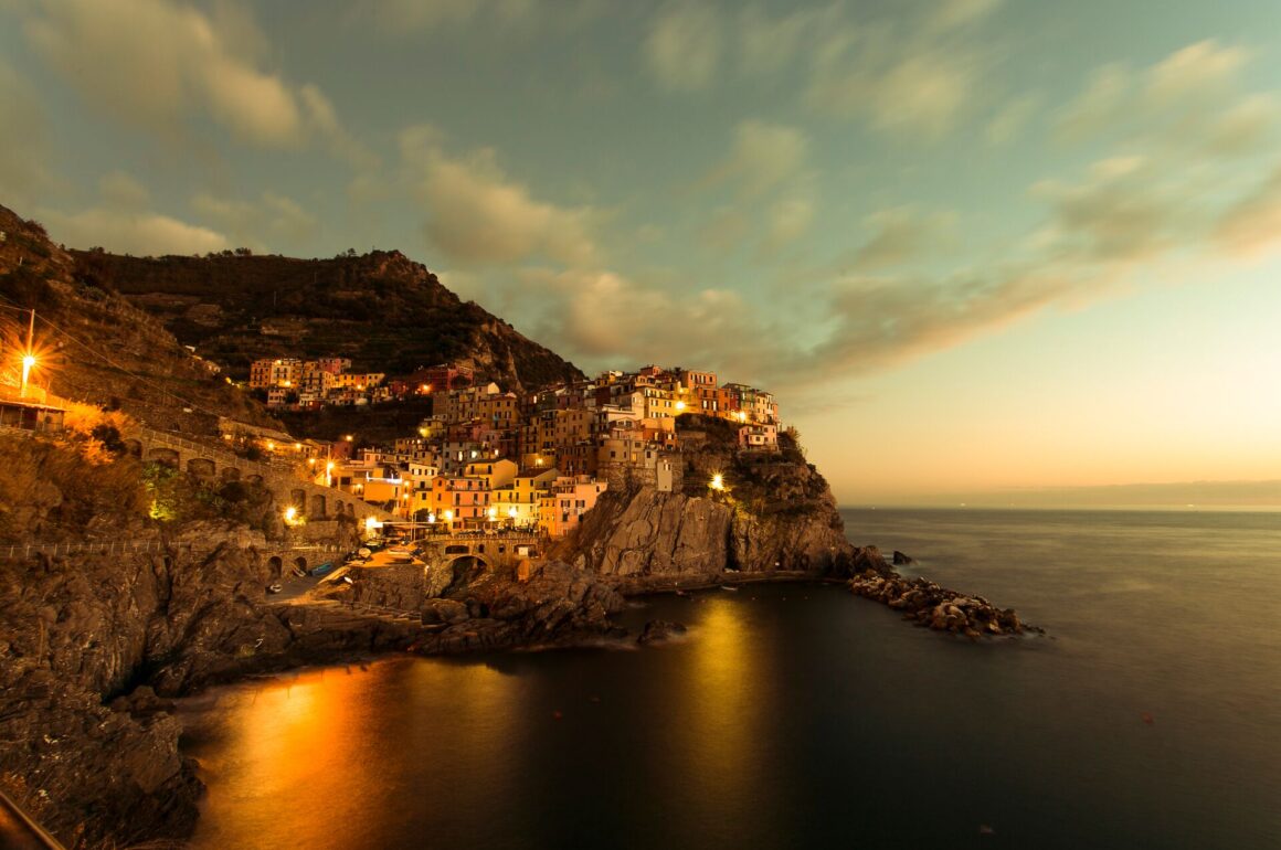 Houses are stacked on the rocks with dark water below on the Cinque Terre at sunset