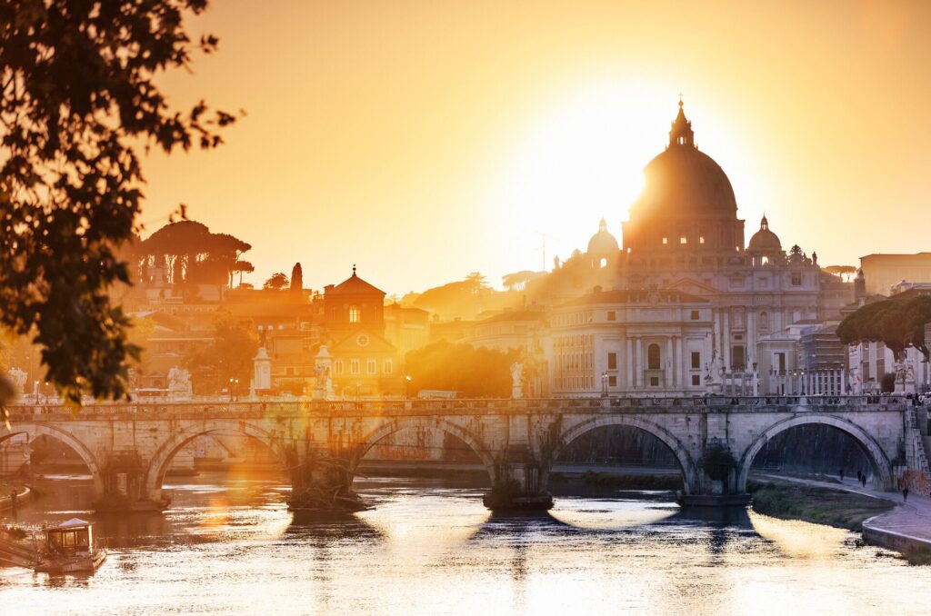 Sunset over Rome showing a river and bridge in front of St Peter Basilica 