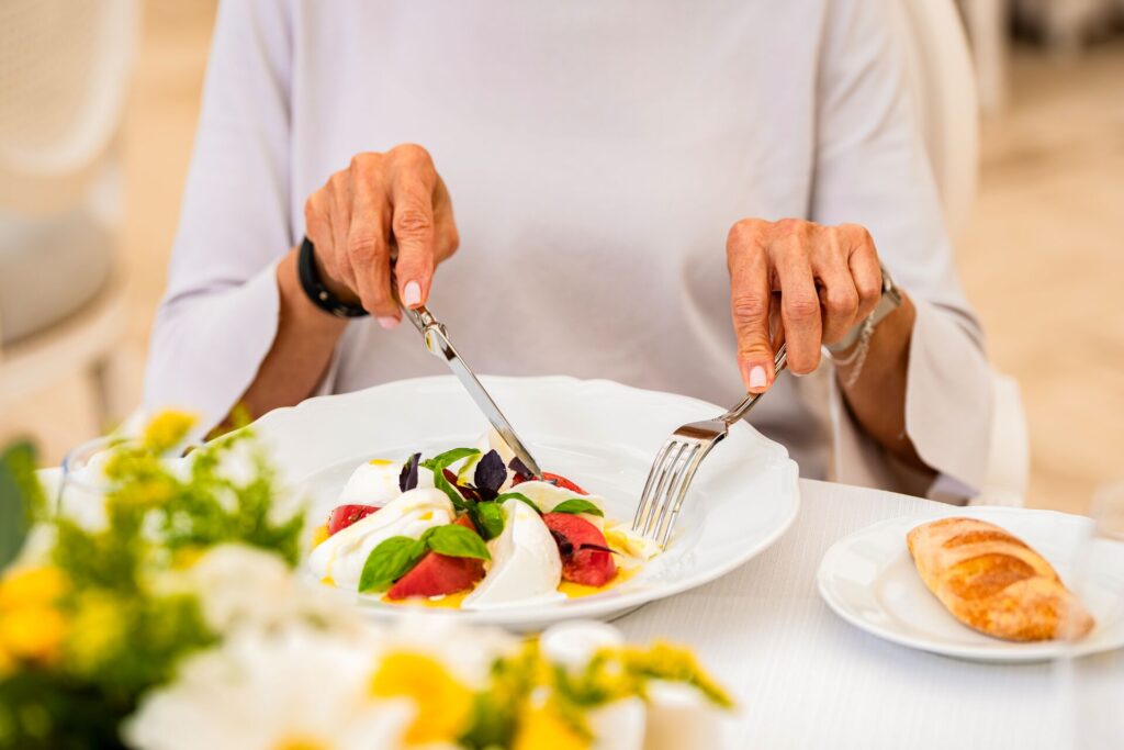 An elegant plate of mozarella and tomatoes with a womans hands holding a knife and fork