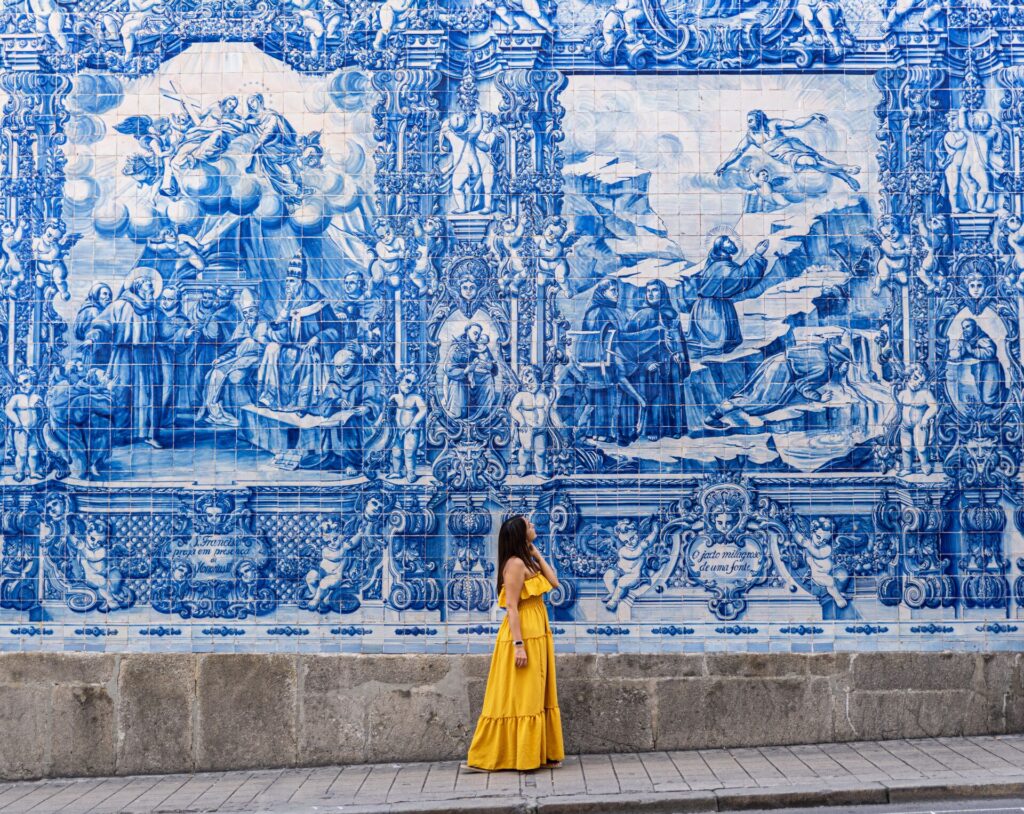 A woman in a yellow dress gazes at a huge blue and white mural painting in Portugal.