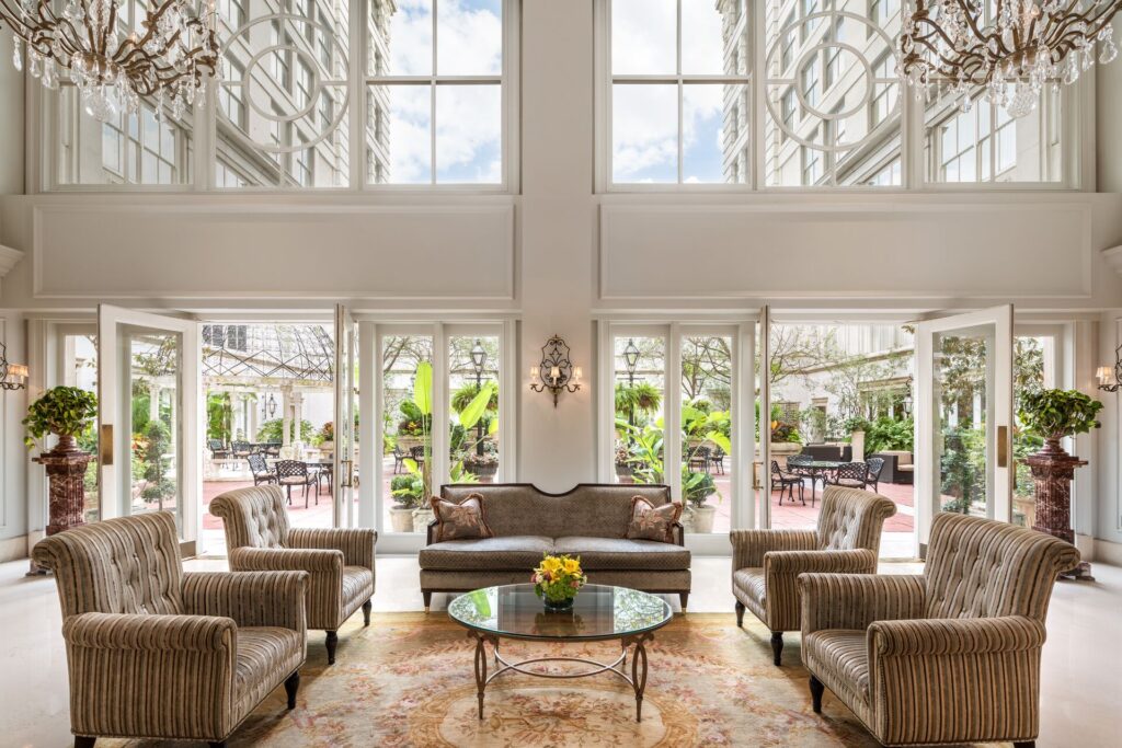 Plush brown chairs, floor to ceiling windows set in white overlooking an indoor garden at the Ritz Carlton in New Orleans.