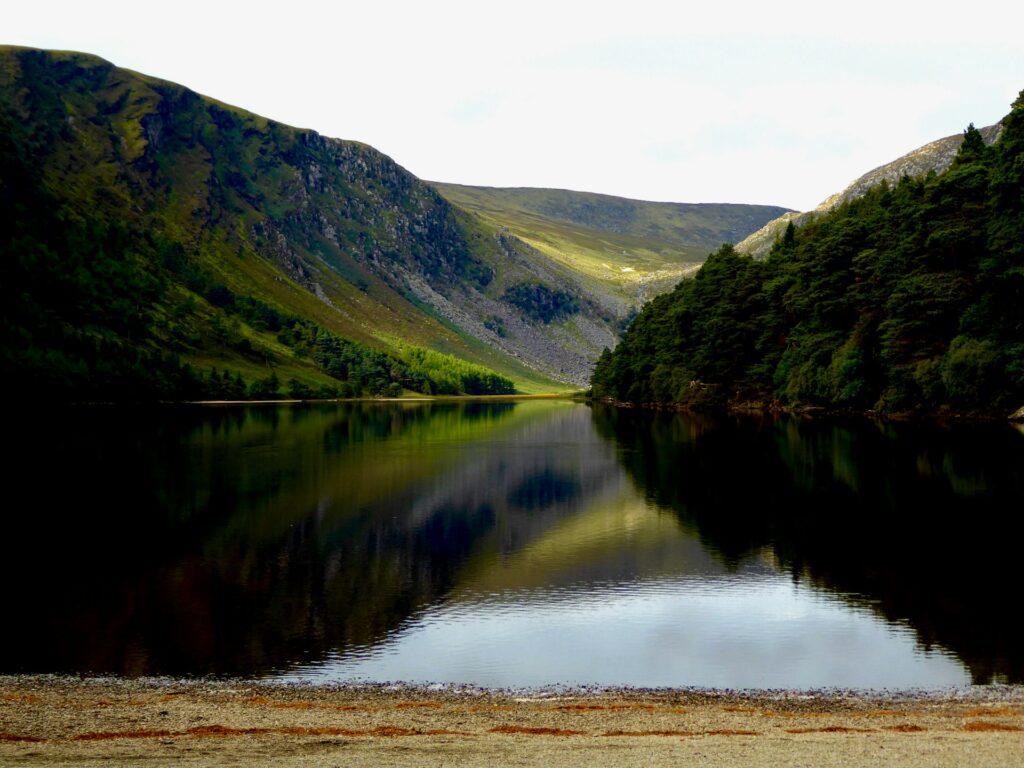 View across a placid lake, reflecting the dark slopes of the valley either side