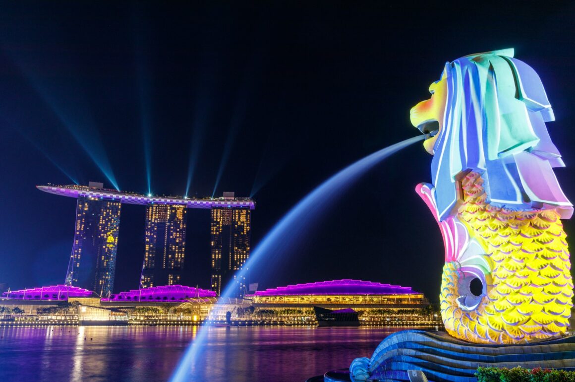 Colourful dragon shaped fountain spouting water in the foreground with futuristic skyscrapers in the background, photographed at night