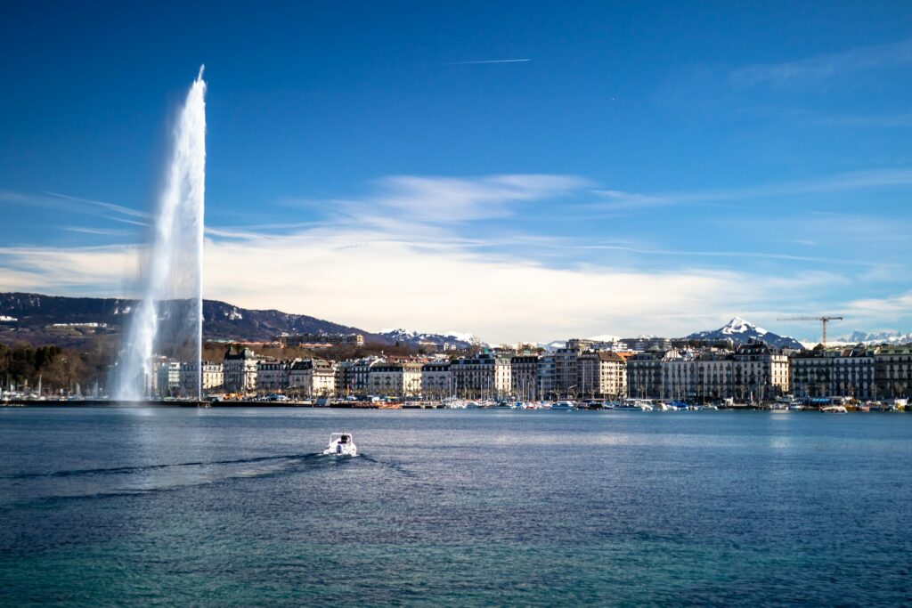 View looking across a large lake, with a large high-spouting fountain in the water and buildings lining the shore